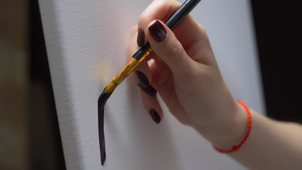 closeup. female hand painting with a brush a black line on a clean white canvas