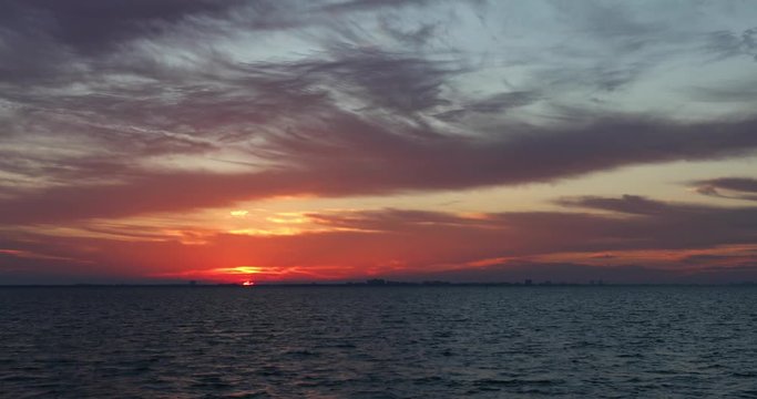 A colorful sunrise paints a cloudy sky with color over San Carlos Bay with Fort Myers Beach, Florida on the horizon in this seamless motion background video time lapse