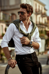 Stylish man wearing sunglasses and white shirt with tied sweater on shoulders
