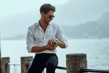 Stylish man in white shirt checking the time over the mountains background - 308845324