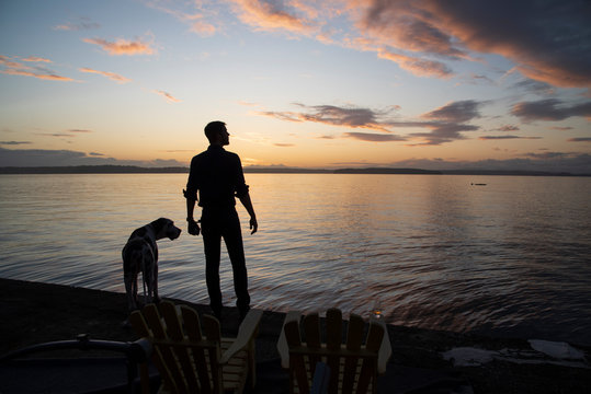 Silhouetted man with dog at sunset, drink on chair