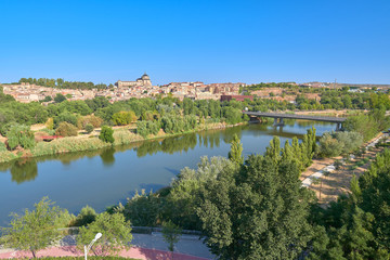 Obraz premium Landscape view of the Tagus river upon arrival in the city of Toledo with the Covachuela neighborhood and the Tavera Hospital in the background, Castilla la Mancha, Spain