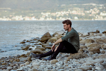Handsome man sitting on the beach lookinag at the lake and relaxing
