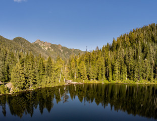 Secluded Kelcema Lake and the surrounding mountain and trees reflecting in the shaded water on a clear summer afternoon in the Mount Baker-Snoqualmie National Forest in Silverton Washington State