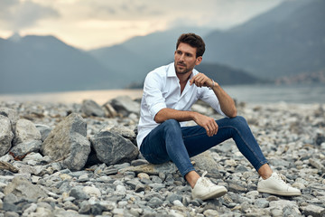 Fashionable male model sitting outdoor near the lake