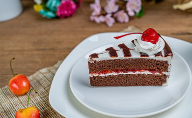 Chocolate cake with white cream and red cherry on white ceramic plate