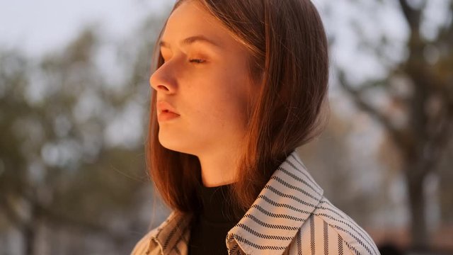 Close up shot of pensive girl in trench coat dreaming near fashion store on city street