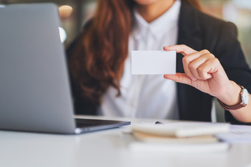 A businesswoman holding and showing a blank business cards while using laptop computer in office