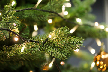 Christmas tree branches close up decorated with garland lights. Festive holiday background with artificial fir tree. Blurred backdrop - Powered by Adobe