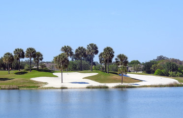 Sand bunkers and palm trees on a golf course bordering on a small pond