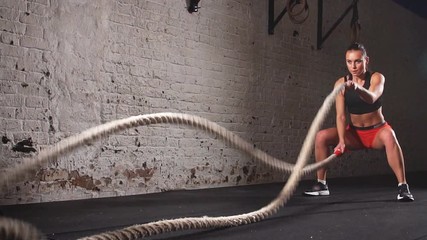 Athletic woman exercises with battle ropes as part of her fitness gym workout. Slow motion - Powered by Adobe