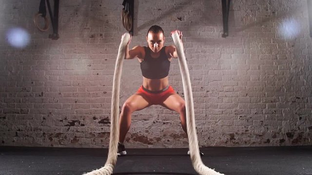 Slow motion of athletic woman with battle ropes exercise in fitness gym. Cross Fit.