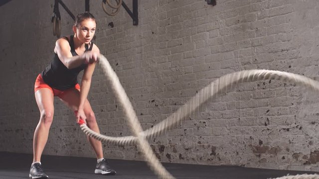 Concept: power, strength, healthy lifestyle, sport. Powerful attractive muscular woman crossfit trainer workout with ropes at gym.
