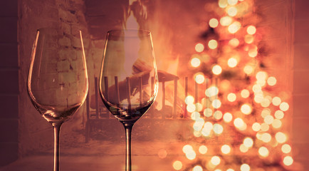 Cozy Christmas evening at home by the fire. Pair of wine glasses next to Christmas tree and warm fire.  