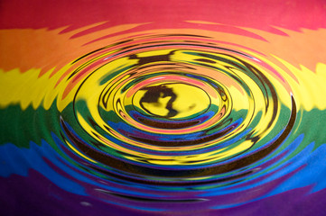 Circular ripples on a water surface reflecting the Gay Pride Extinction Rebellion flag and logo