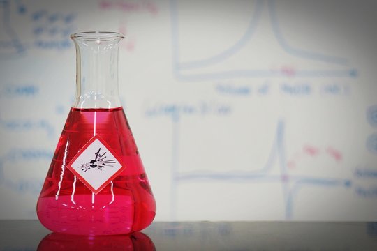 Erlenmeyer flask with Pink liquid and chemical hazard warning symbols labels (explosive sign) on whiteboard with chemical learning background.
