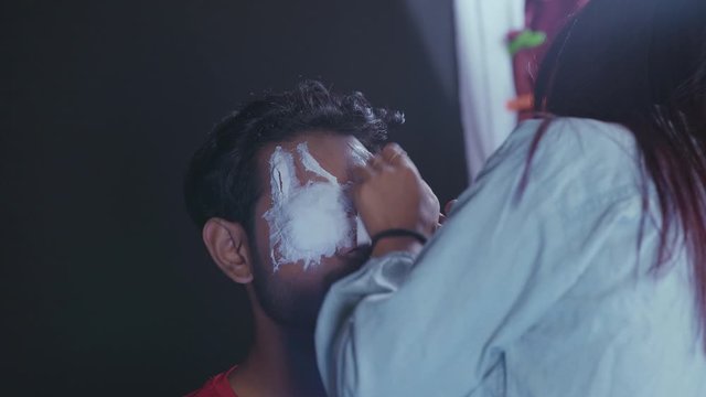 Make up artist preparing man's face and putting white prosthetic insert to make a Halloween mask 