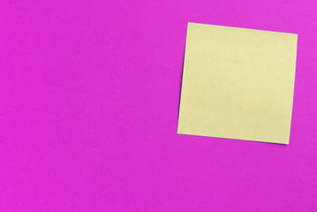 Square yellow sticker note on a bright pink background close up