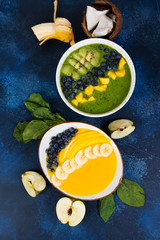 Fototapeta na wymiar Two cups of different smoothie bowl of green and yellow fruits. The concept of healthy eating. Vertical photo. Top view.
