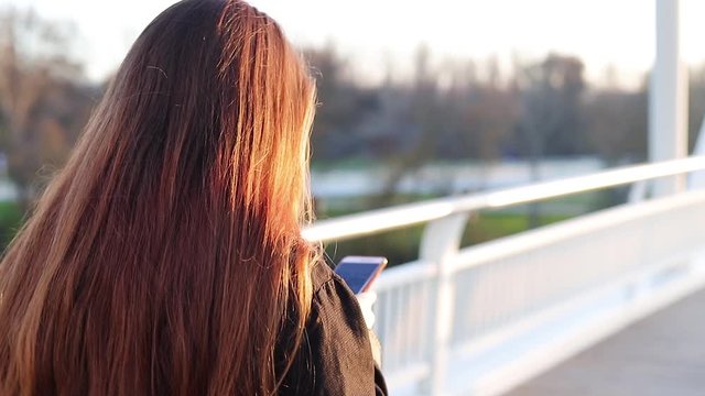 millennial young woman walking in a footbridge with her smartphone at sunset
