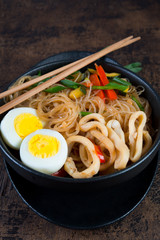 Stir fry with glass noodles, vegetables and seafood in Asian style on a dark wooden background. Vertical photo.