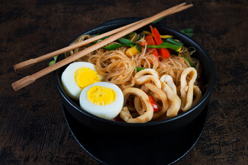 Stir fry with glass noodles, vegetables and seafood in Asian style on a dark wooden background. Horizontal photo.