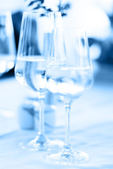 A glass of white wine and a glass of water on a white tablecloth toned in classic blue. Light airy backdrop, vertical