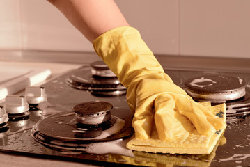A hand in a yellow rubber glove washes a gas stove. Spring cleaning concept. Brown color toned