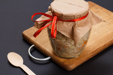 Fermented cabbage with herbs and spices in glass can on the black background
