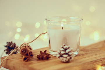 White burning candle with decorations and garland lights in bokeh on a wooden table. Cozy home and hygge concept