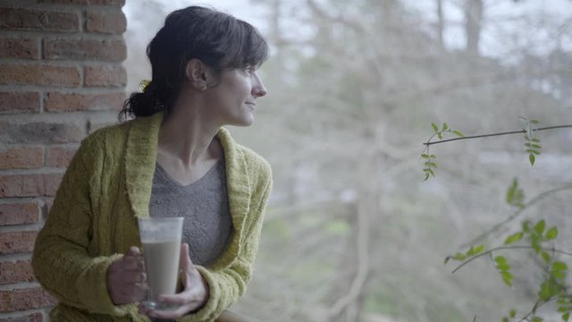 Middle Agged Woman Drinking Coffee On House Balcony, Unfocused Background