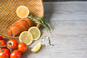 Grilled salmon steak on vintage wooden board with fork, olive oil, vegetables, herbs and spices on dark concrete background. Raw salmon fillet with vegetables, spices and lemon on wooden table.