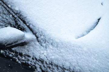 The car is covered in snow. Snow falls.