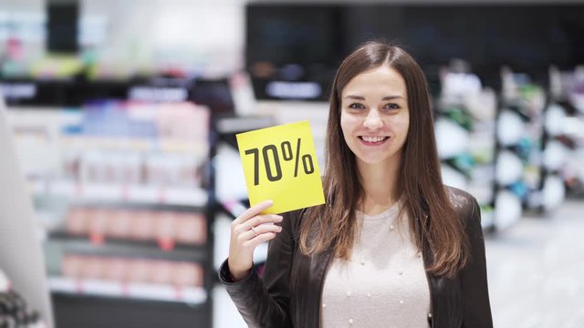 Woman at cosmetics store shows thumb up and discount sign, big sale, she shocked