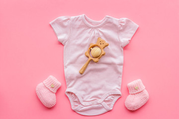 Pink bodysuit for baby girl near children's things on pink background top-down