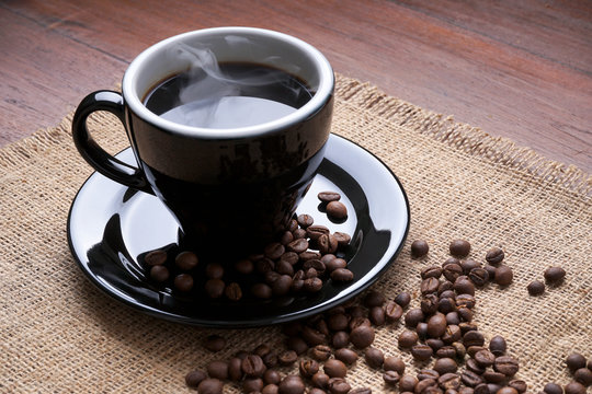 Black cup of a hot black coffee with coffee beans on jute