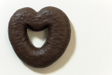 Chocolate gingerbread in the shape of a heart on a background of white texture paper. Place for text (copy-space) on the right.
