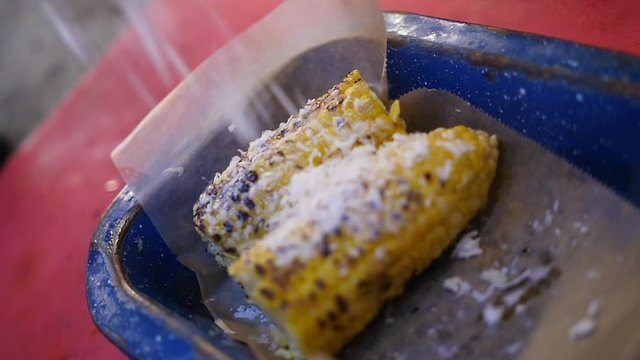 Close up of a chef garnishing the tasty corn on the cob with grated cheese