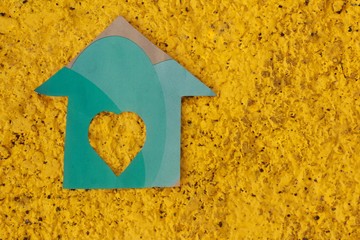 Casa de papel verde  ,con fondo amarillo, sujetado de una mano.