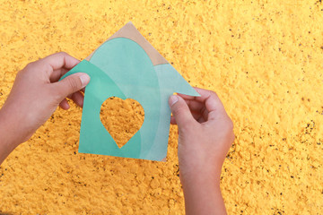 Casa de papel verde  ,con fondo amarillo, sujetado de una mano.