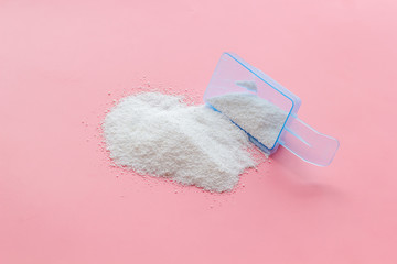 Household chemicals. Washing powder in plastic spoon on pink background
