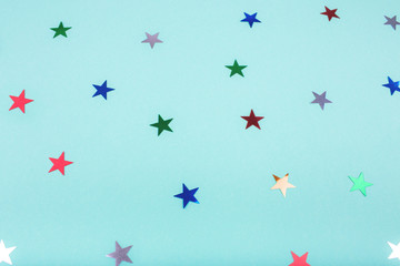 Fototapeta premium Multicolored, glitter stars on mint color background. For Christmas and New year day. Copyspace for text. Top view, flat lay. Holiday backdrop.