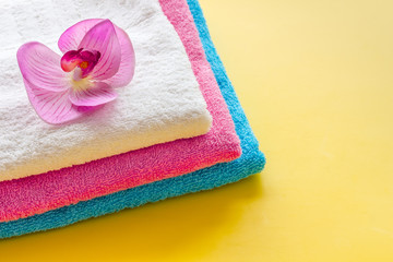 Obraz na płótnie Canvas Clean towels - stack of laundred linen with orchid flower - on yellow background copy space