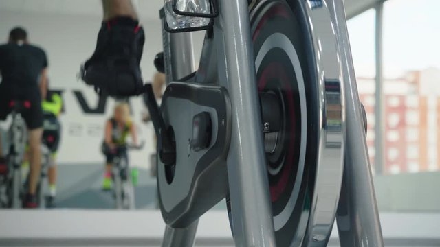 Close-up Partial View Of Human Foot Spinning Pedal On Flywheel. Cropped Shot Of Person Training On Spin Bike In Cycling Class