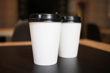 Several, two paper white cups with a plastic black lid for takeaway coffee on a black background of the table in the cafe.Close up view of disposable paper coffee Cup in cafe