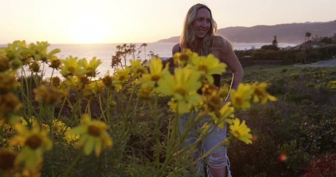 Woman revealed behind yellow flowers at sunset with ocean in background. Filmed at Big Dume in Malibu, California. Shot on RED Dragon.
