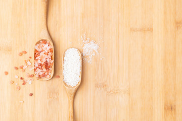 Closeup & top view of beautiful pinkish Himalayan salt rock mined from the salt range mountains and sea salt that evaporation of ocean water lots of iodine in a wooden tea scoop on table.