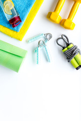Fitness background - dumbbells, jump rope, sport carpet, water bottle - on white top-down frame copy space