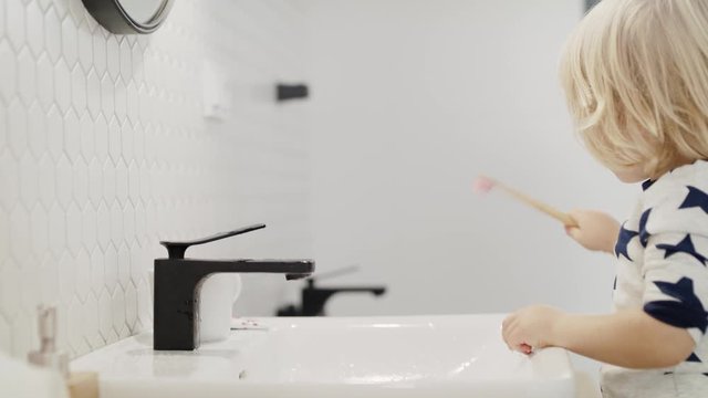 Small blond boy indoors in bathroom, brushing teeth and washing.