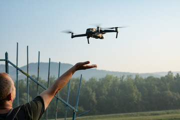 A man behind a metal fence takes a flying drone on his arm. Concept: let the drone fly to freedom....